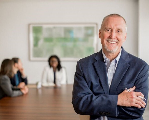 An attorney smiling at the camera while his team meets in the background